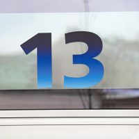Modrá plotrovaná číslice 13 na skleněné výplni, označení čísla vchodu O2 Universum